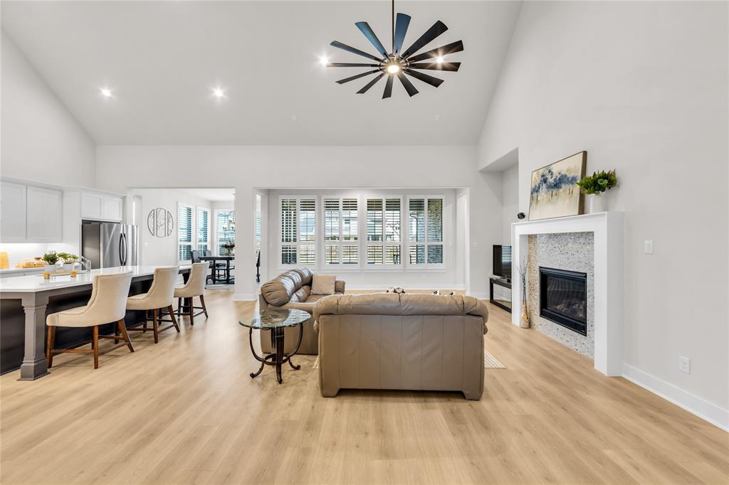 Open-concept interior featuring vaulted ceilings, wood-finish flooring, a contemporary ceiling fan, and a fireplace with a decorative stone surround