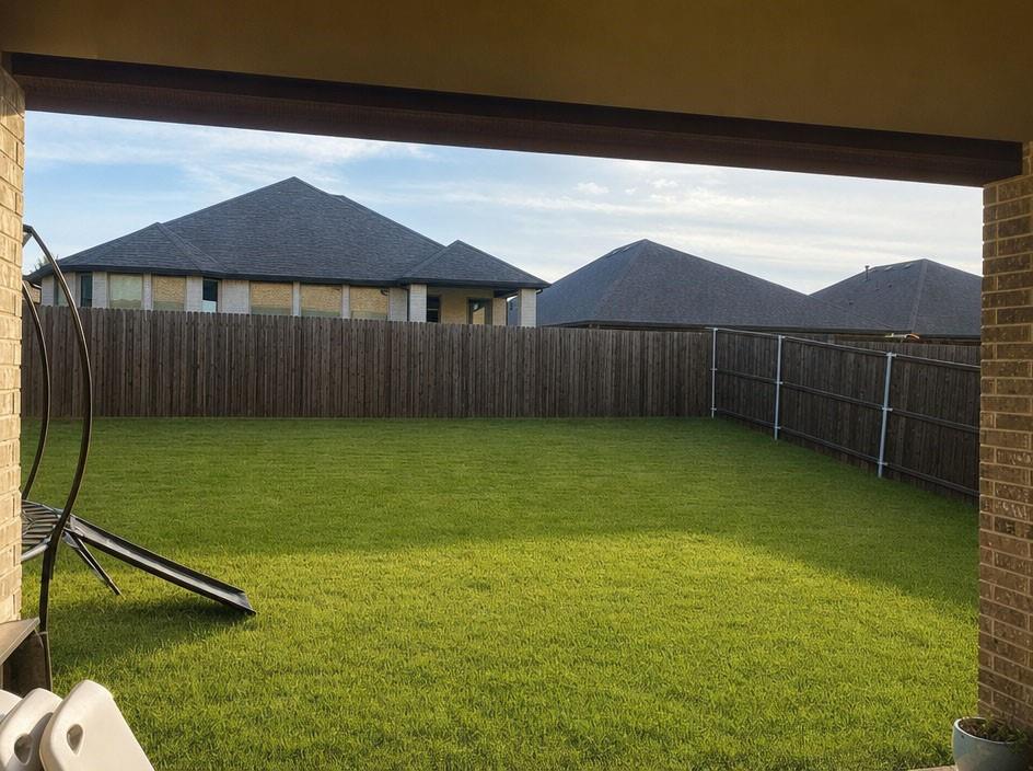 Backyard featuring a manicured lawn, wood-slat perimeter fencing, and a covered brick-columned patio Backyard featuring a manicured lawn, wood-slat perimeter fencing, and a covered brick-columned patio