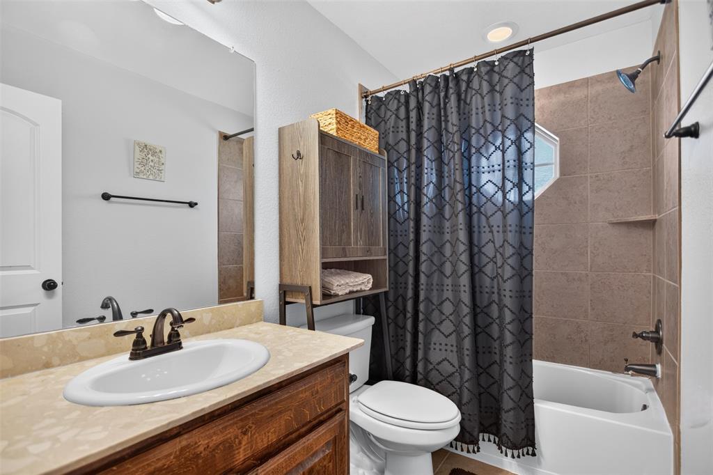 Bathroom featuring a wood-finish vanity with a stone-composite countertop, integrated oval basin, and oil-rubbed bronze hardware, complemented by a tiled shower surround and a fixed octagonal window