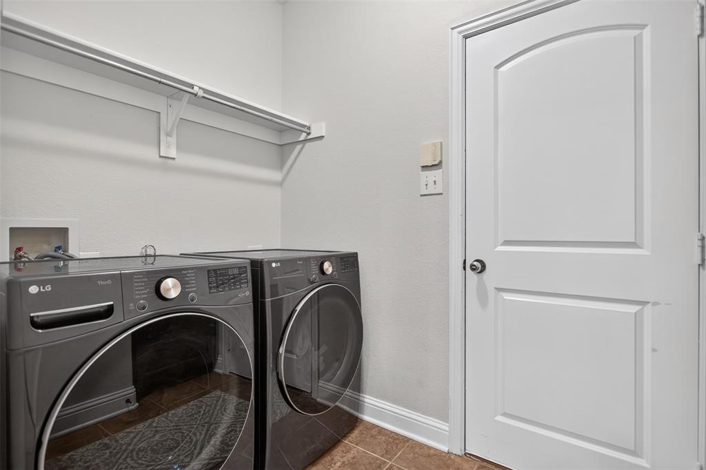 Laundry room featuring a single-panel arched interior door, installed wall-mounted shelving with integrated hanging rod, ceramic tile flooring, and recessed laundry hookups