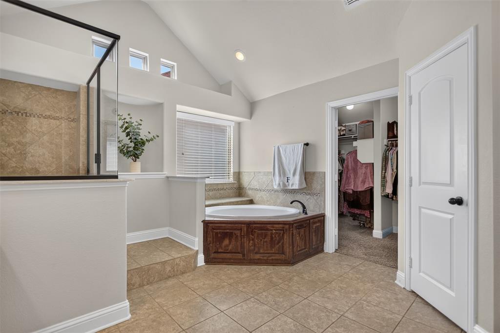 Vaulted ceilings, corner soaking tub with wood-finish cabinetry, ceramic tile flooring, glass-enclosed shower with tile surround, and built-in recessed wall niche