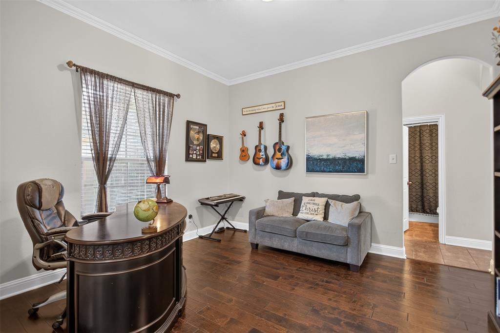 Room featuring wood-finish flooring, crown molding, and an arched entry