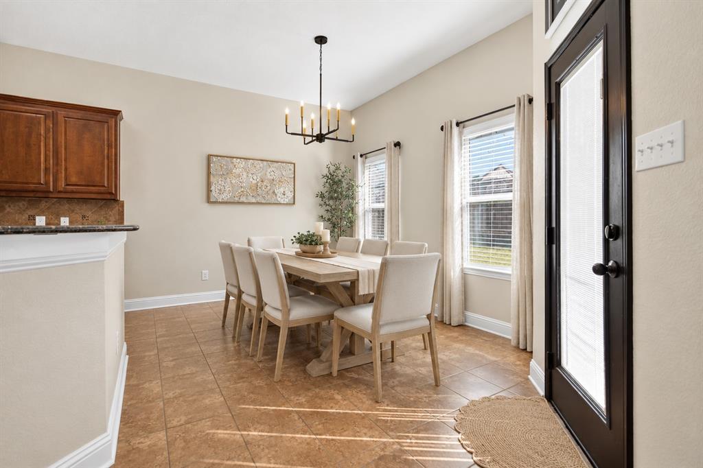 Dining area featuring ceramic tile flooring, a multi-light metal chandelier, and windows with neutral-tone treatments, accented by a door with dark trim
