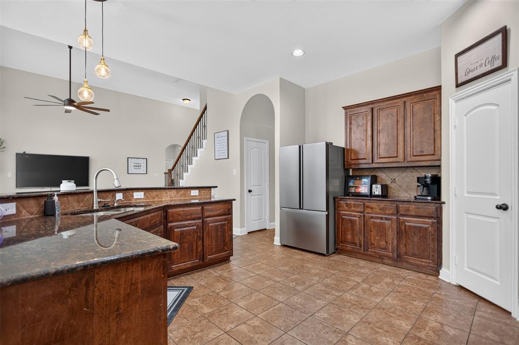 Kitchen featuring dark wood cabinetry, stone-finish countertops, tile flooring, tile backsplash, and multi-light pendant fixtures