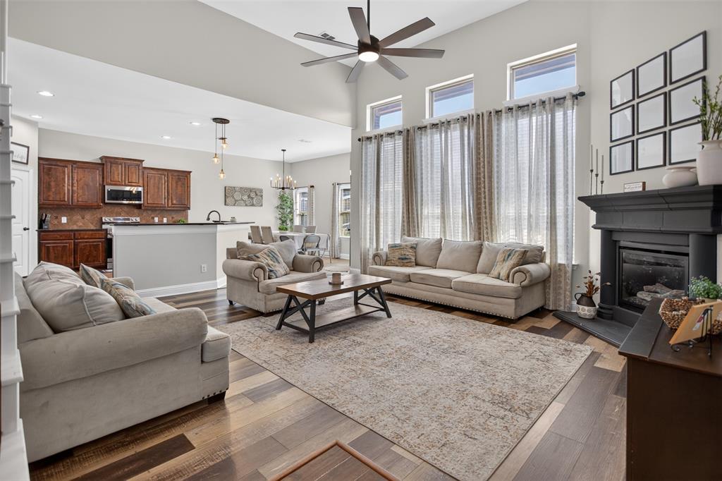 Vaulted ceiling with a multi-blade ceiling fan, expansive windows, dark-finish fireplace surround, and wood-finish flooring