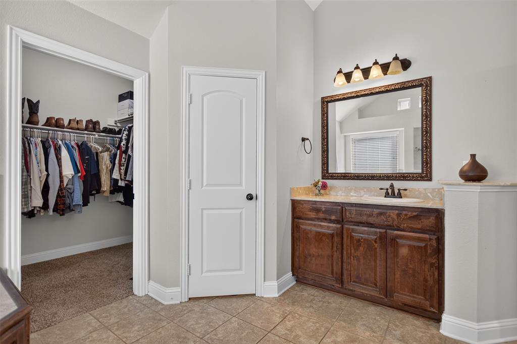 Vanity featuring stained wood cabinetry, stone-finish countertop, undermount sink, and wall-mounted light fixture
