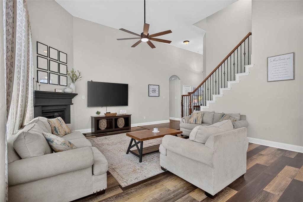 Vaulted ceiling with an integrated multi-blade ceiling fan, dark wood-finish flooring, fireplace with a painted mantel, and a staircase featuring metal balusters