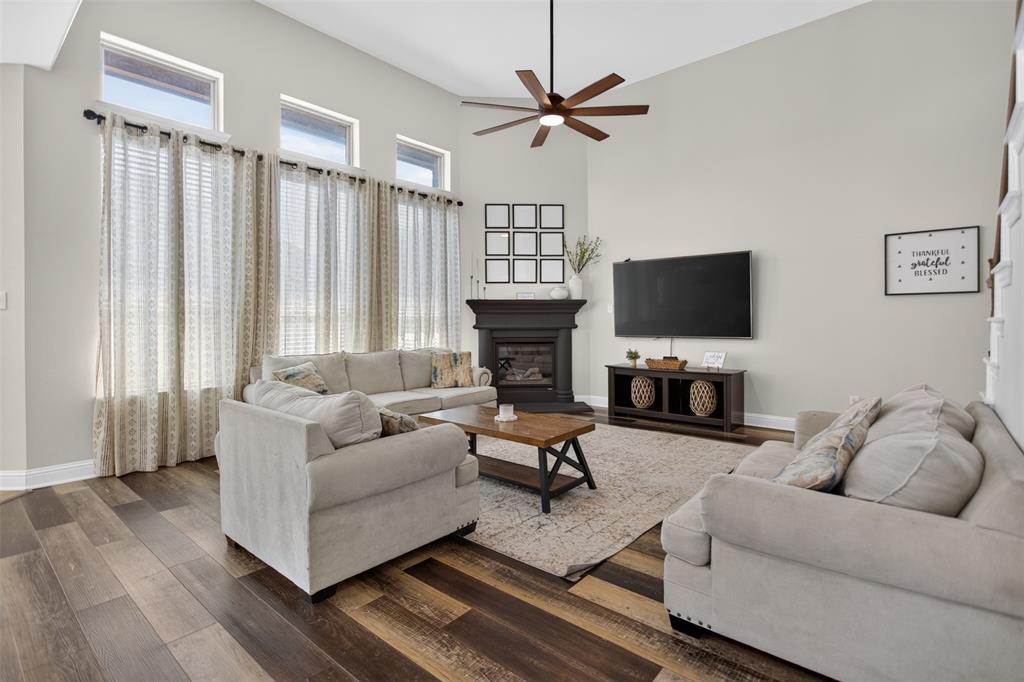 Living area featuring high ceilings, wood-finish flooring, transom windows, and a dark-toned fireplace surround with a ceiling fan