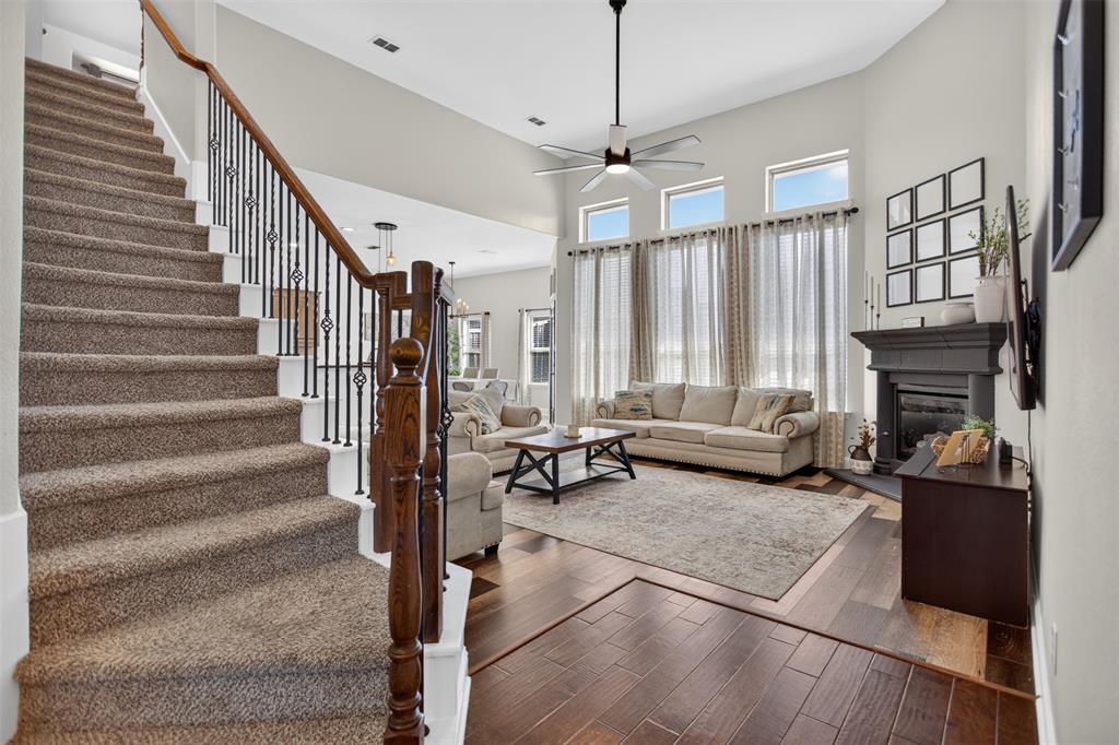 High-ceiling living area featuring wood-finish flooring, a dark-toned fireplace mantel, a multi-pane window configuration, and a staircase with wrought iron spindles and a stained wood banister