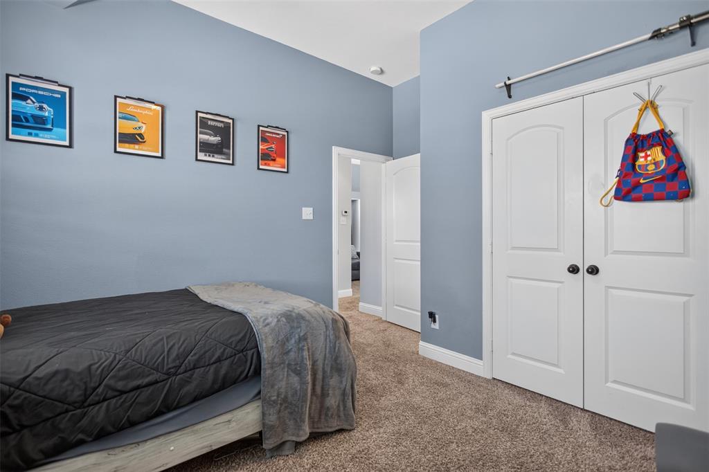 Neutral wall-toned room featuring plush carpeting, dual-panel closet doors with matte black hardware, and an exposed overhead sliding track system