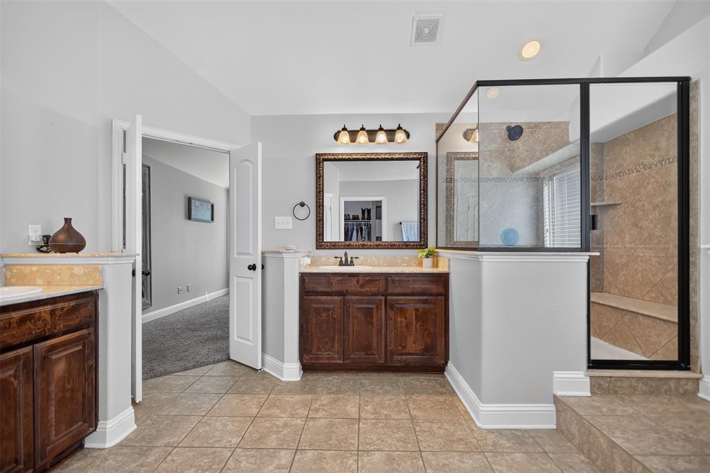 Bathroom featuring dual dark wood vanities with stone countertops, a large framed mirror, and a glass-enclosed shower with tiled walls and a built-in bench