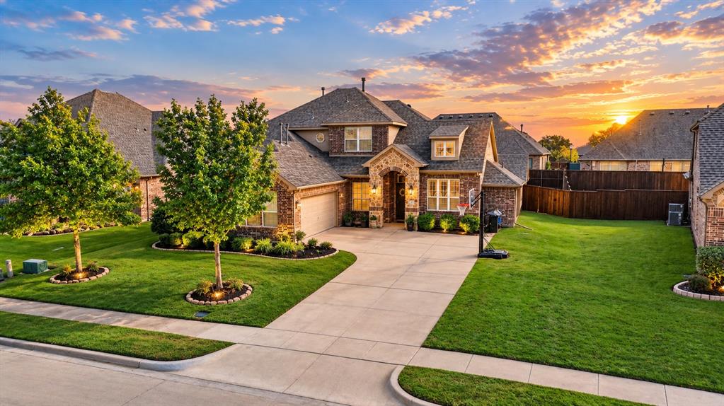 Brick exterior with stone veneer accents, multi-gabled roofline, concrete driveway, and landscaped front lawn with mature trees