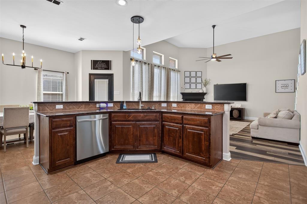 Kitchen featuring dark-toned wooden cabinetry, dark stone countertops, stainless steel dishwasher, tile flooring, and vaulted ceilings with pendant lighting