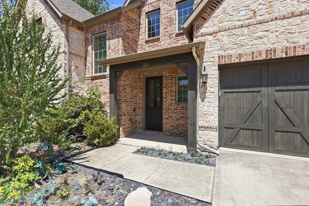 Exterior facade featuring masonry stone and brick veneer, covered entryway, wood-finish garage door, and metal-framed windows