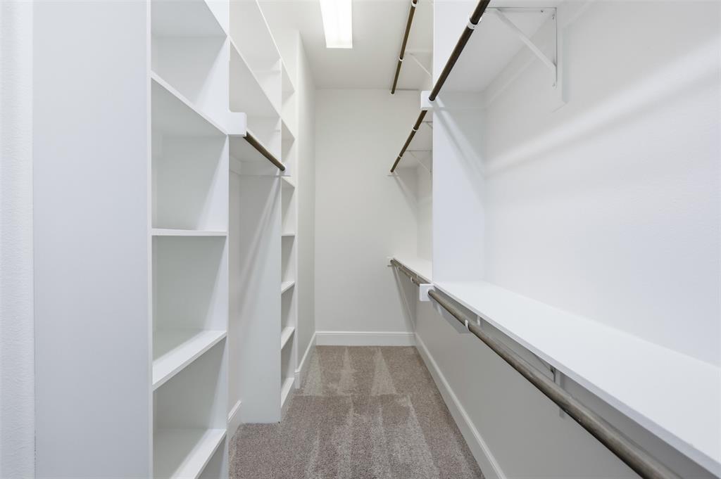 Walk-in closet featuring white built-in shelving, tiered hanging rods, and wall-to-wall carpeting
