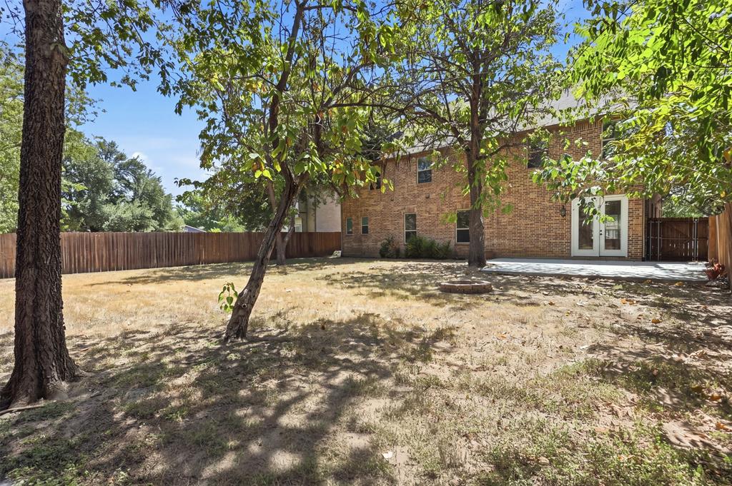 Brick exterior featuring a concrete patio, wood privacy fencing, and mature trees