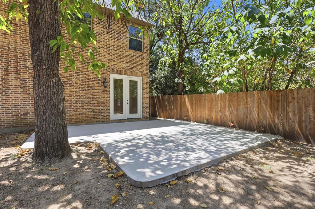 Exterior brick facade featuring a concrete patio, double glass-panel doors, and a wood privacy fence