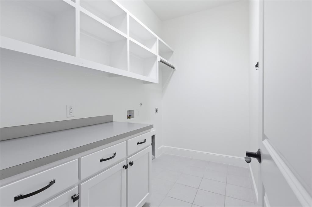 Utility room featuring white shaker-style cabinetry, matte black hardware, grey solid-surface countertops, open wall shelving, and neutral floor tile
