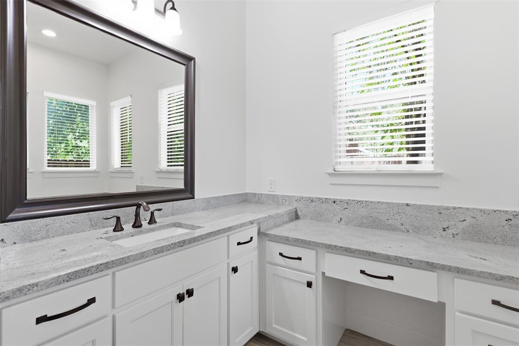 Bathroom vanity featuring white shaker-style cabinetry, light-toned stone countertops, a rectangular undermount sink with a widespread faucet, a large framed mirror, and matte black hardware