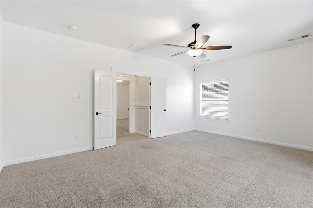Neutral-toned carpeted flooring, white interior walls, ceiling fan with integrated lighting, and white double doors featuring matte black hardware