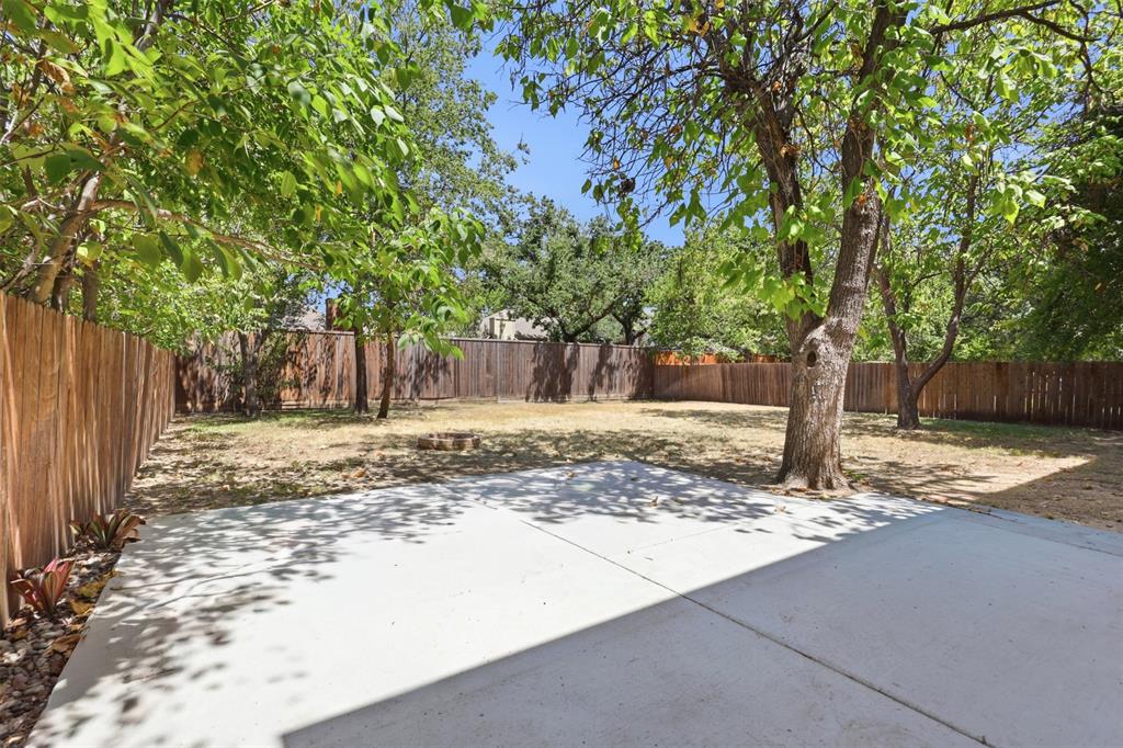 Backyard featuring a concrete patio, wood privacy fencing, and mature trees