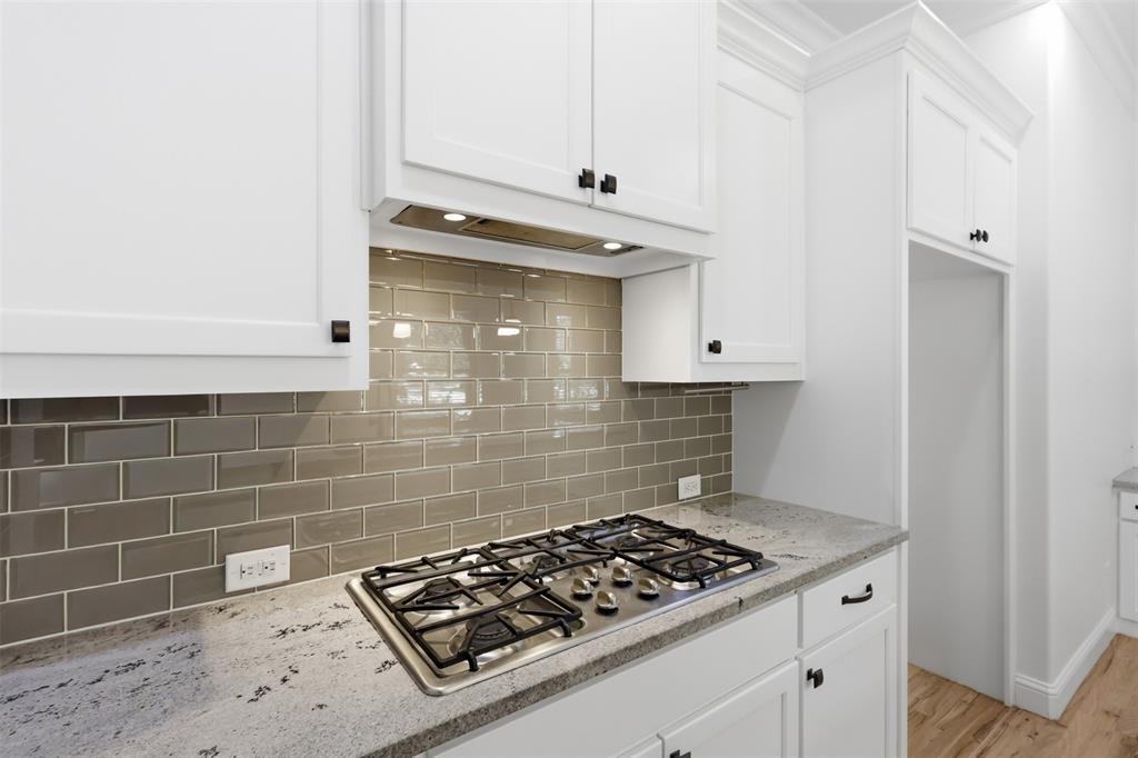 Kitchen featuring white Shaker-style cabinetry, neutral subway tile backsplash, stone countertops, and a built-in stainless steel gas cooktop
