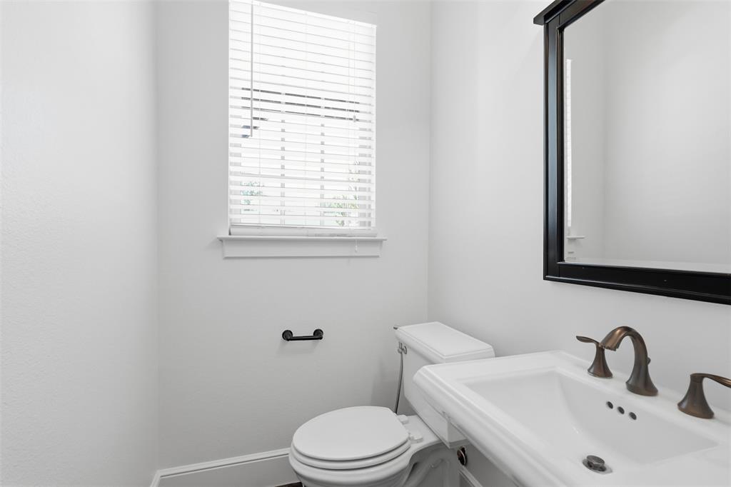 Bathroom featuring a white pedestal sink, oil-rubbed bronze widespread faucet, framed wall mirror, and horizontal slat window blinds