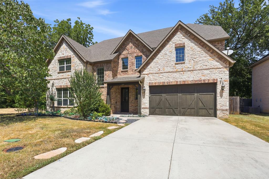 Two-story exterior featuring light stone and brick masonry, a multi-gabled roofline, and an attached multi-car garage with wood-finish doors