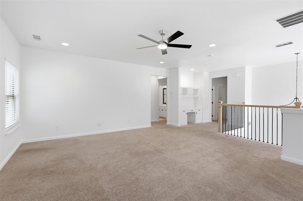 Open living space featuring recessed lighting, a ceiling fan with integrated light, carpeted flooring, a built-in desk with overhead cabinetry, and an open metal spindle railing