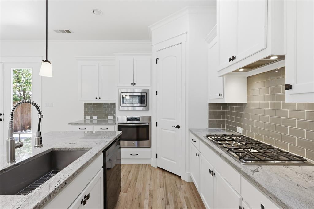 Kitchen featuring shaker-style cabinetry, light-toned stone countertops, a subway tile backsplash, stainless steel built-in appliances, and wood-finish flooring