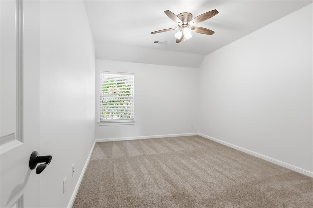 Neutral-toned carpeting, vaulted ceiling, multi-blade ceiling fan with integrated lighting, and a single window with horizontal blinds