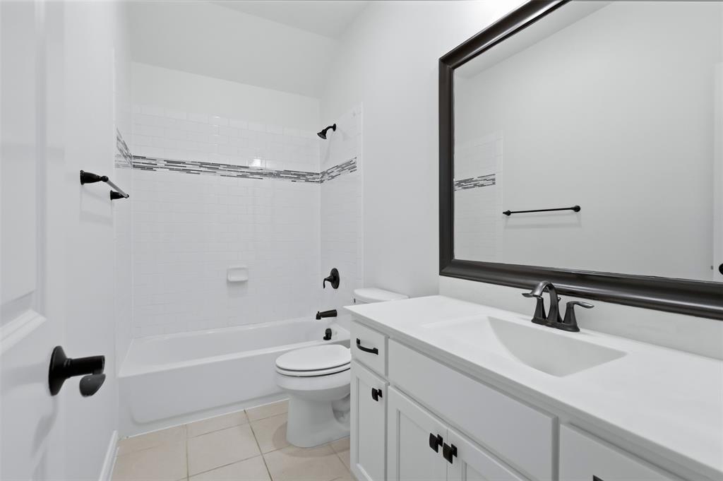 White vanity with integrated countertop and sink, matte black hardware, framed wall mirror, and tub-shower combination featuring decorative mosaic tile inlay