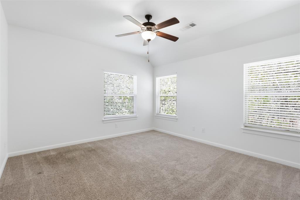 Neutral carpeted flooring, vaulted ceiling, and three windows featuring blinds, centered by a ceiling fan with integrated lighting