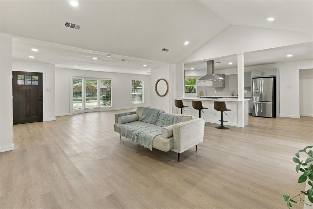 Open-concept interior featuring vaulted ceilings, wood-finish flooring, recessed lighting, a bay window, and a kitchen peninsula with a stainless-steel range hood