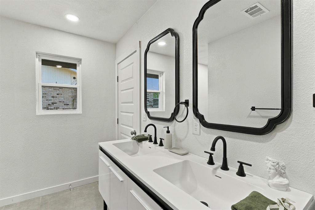 Dual-sink vanity featuring a solid-surface countertop, matte black widespread faucets, scalloped-edge mirrors, and white cabinetry