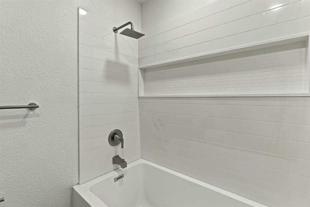 Shower area featuring white subway tile surround, built-in recessed storage niche, rectangular rainfall shower head, and metallic finish plumbing fixtures
