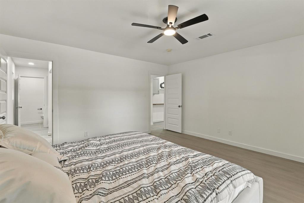 Neutral-toned interior space featuring wood-finish flooring, a multi-blade ceiling fan with integrated lighting, and white five-panel interior doors