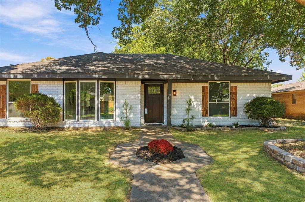 Painted brick exterior featuring a multi-pane front door, shutter-style window accents, a low-pitched roofline, and a stone-bordered front garden bed