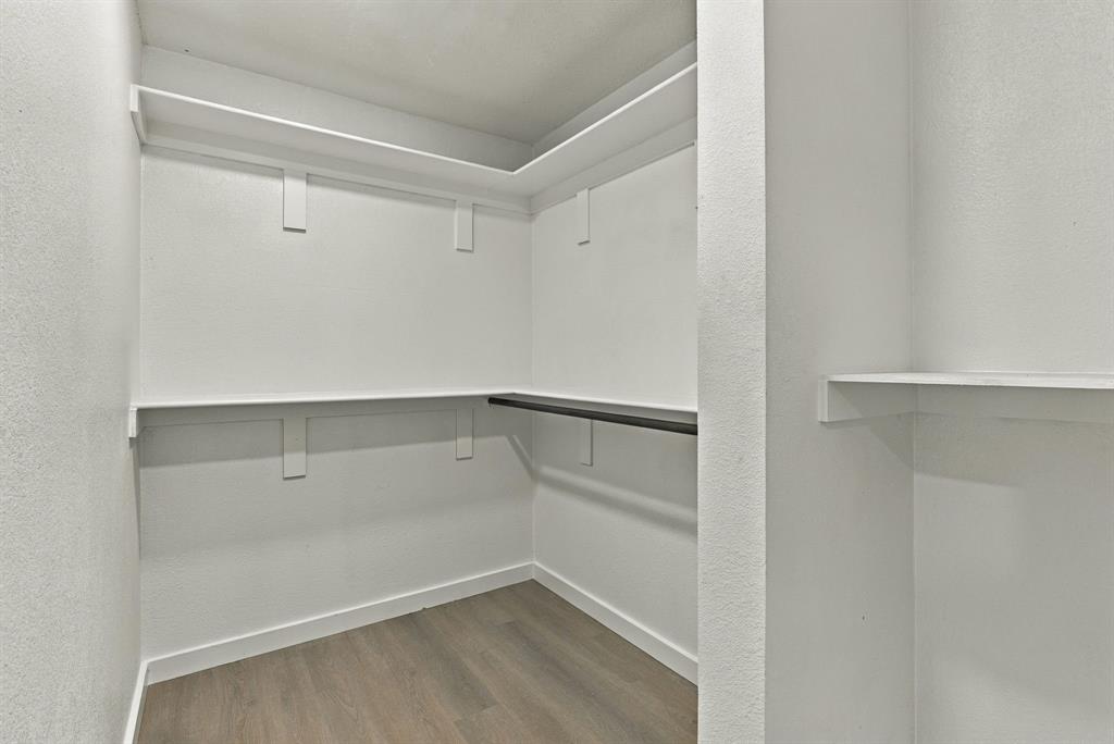 Walk-in storage space featuring wood-finish flooring, multi-level shelving, and a built-in hanging rod
