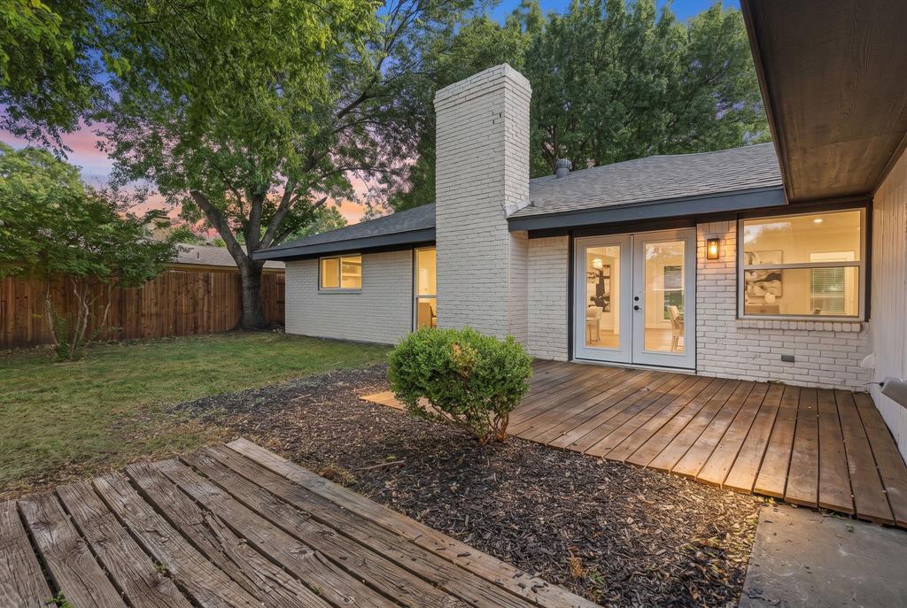 Exterior brick facade with a central chimney, featuring dual wood deck surfaces, double glass-panel doors, and a fenced backyard
