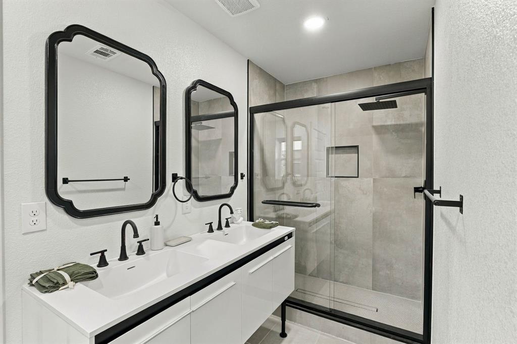 Floating dual-sink vanity with matte black faucets and hardware, expansive wall-mounted mirrors with black frames, and a walk-in shower featuring large-format tile surround and matte black fixtures