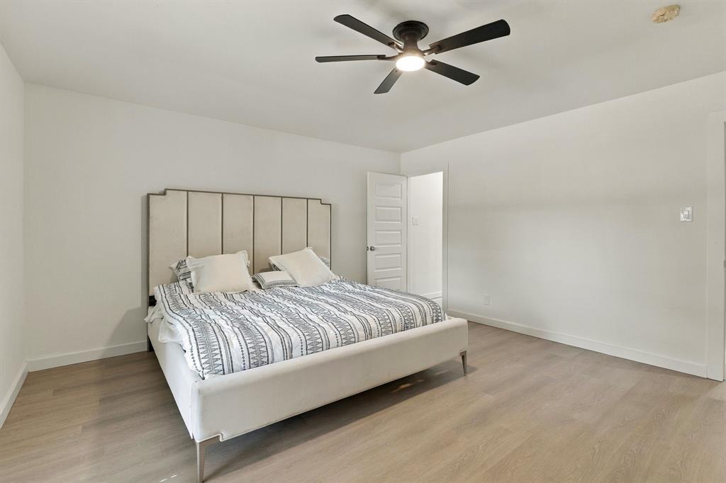 Room featuring wood-finish flooring, a matte black multi-blade ceiling fan with integrated lighting, and a multi-panel interior door