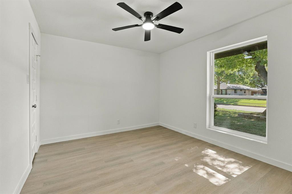 Room featuring wood-finish flooring, a matte black ceiling fan with integrated lighting, neutral wall paint, and a single-pane window