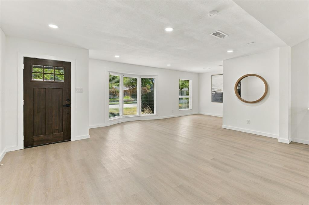Open-concept interior featuring light-toned wood-finish flooring, recessed lighting, a bay window, and a dark-stained wood entry door with glass pane detailing