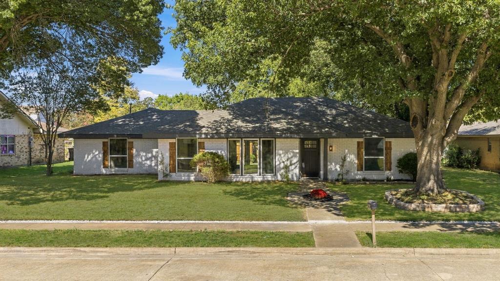 Single-story residence featuring a painted brick exterior, dark-finished shutters, multi-pane windows, a hipped roofline, and established mature trees