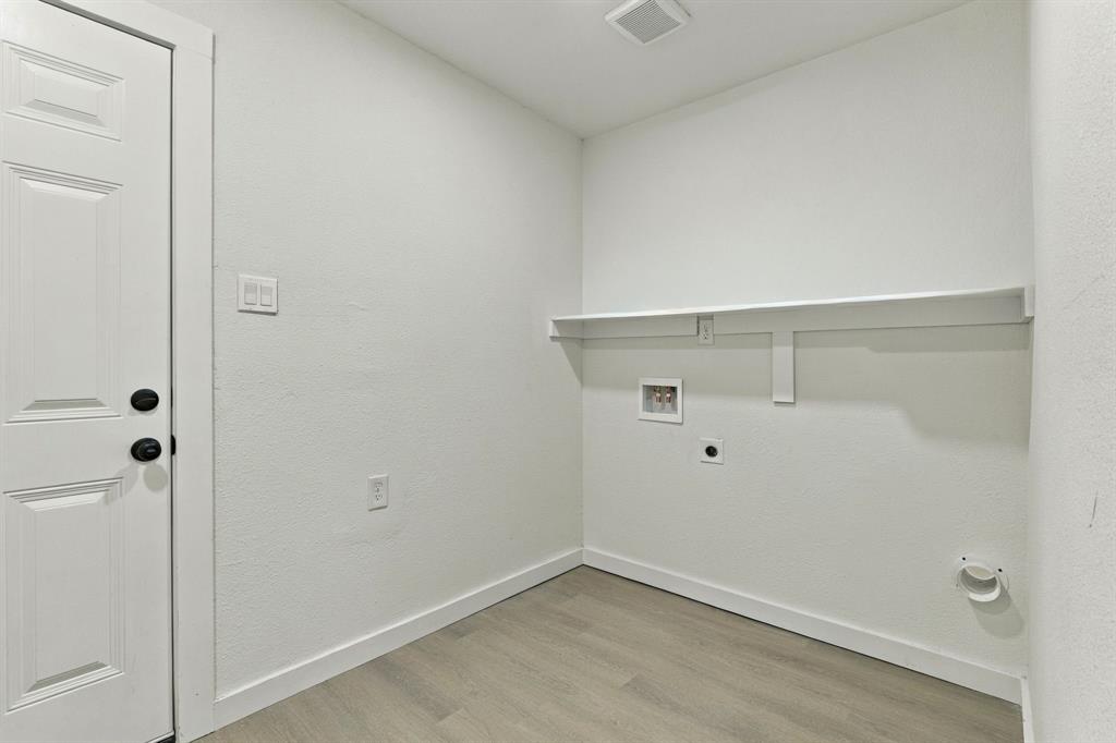 Laundry area featuring wood-finish flooring, a wall-mounted shelving unit, and dedicated utility connections