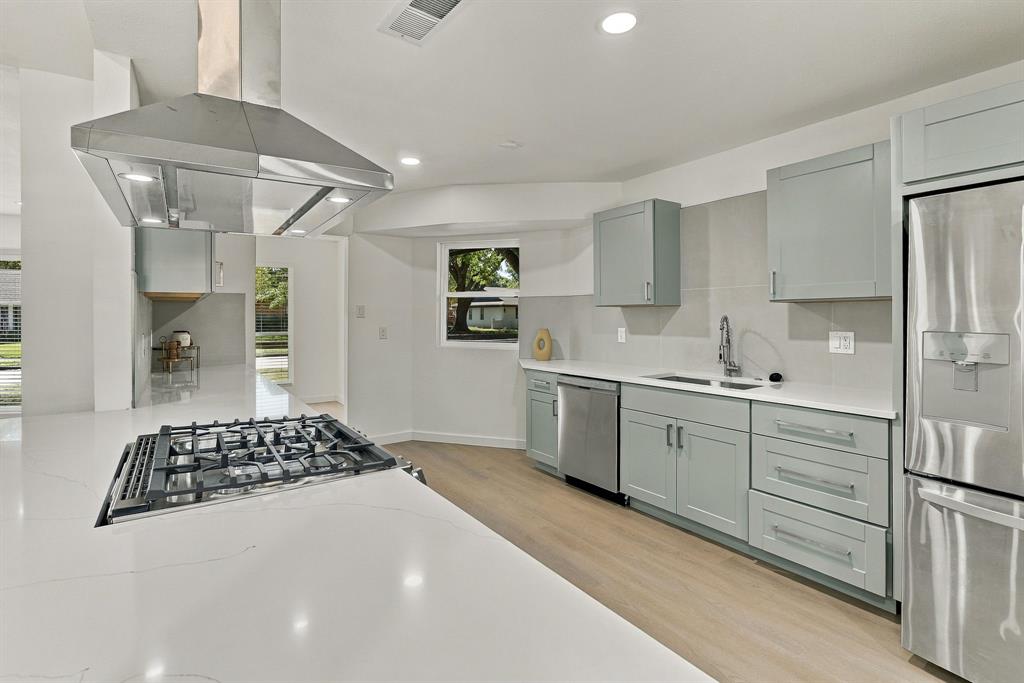 Kitchen featuring light-toned cabinetry, quartz countertops, stainless steel appliances including a gas cooktop with an overhead range hood, and wood-finish flooring