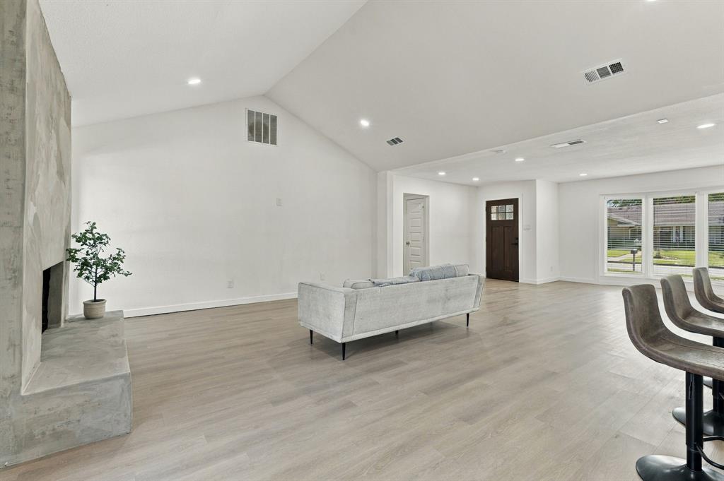 Vaulted ceiling, stone-surround fireplace, wood-finish flooring, recessed lighting, and large windows
