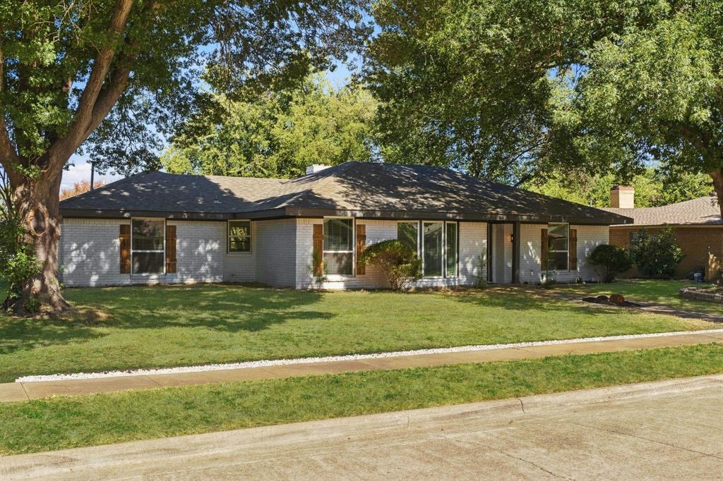 Single-story ranch exterior featuring painted brick siding, a hip roof, multi-pane windows with wooden shutters, and a concrete front walk