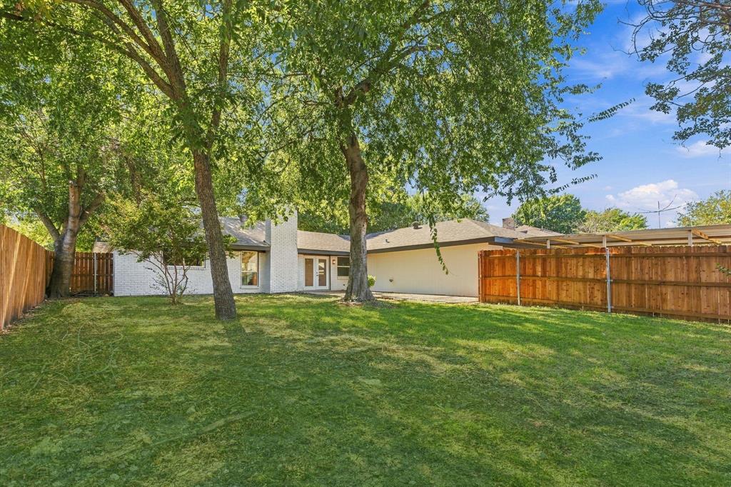 Backyard featuring a grass lawn, mature trees, wood privacy fencing, and an attached covered patio